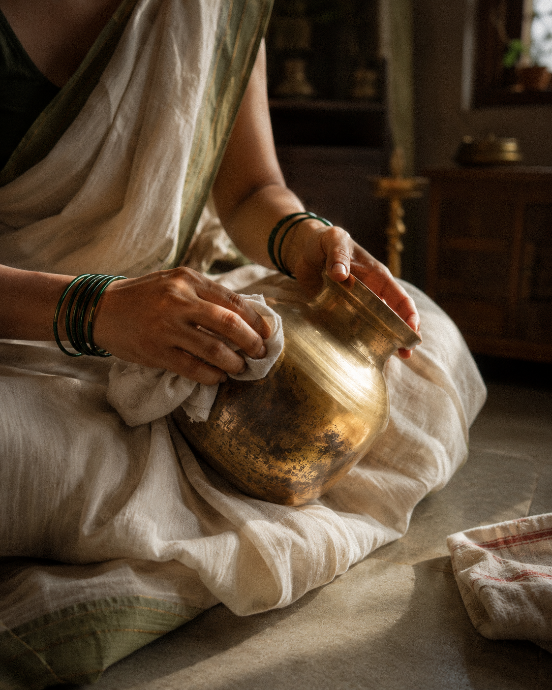 A woman carefully polishing an old brass vessel