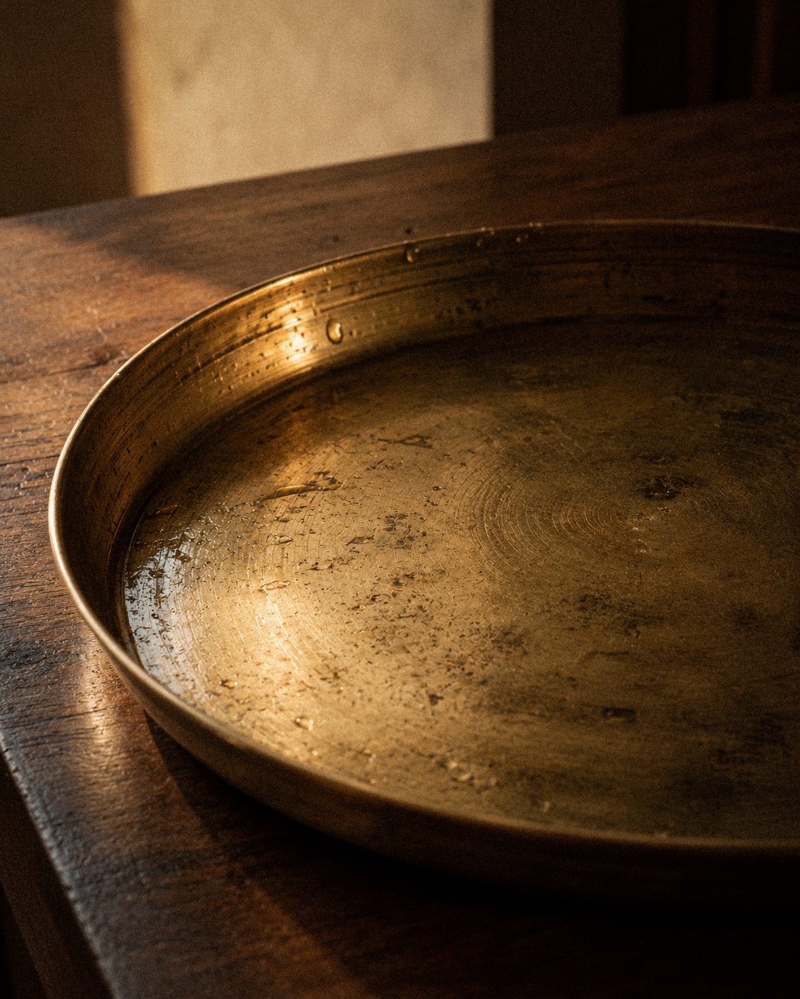 An aged brass plate resting on a wooden table in warm light